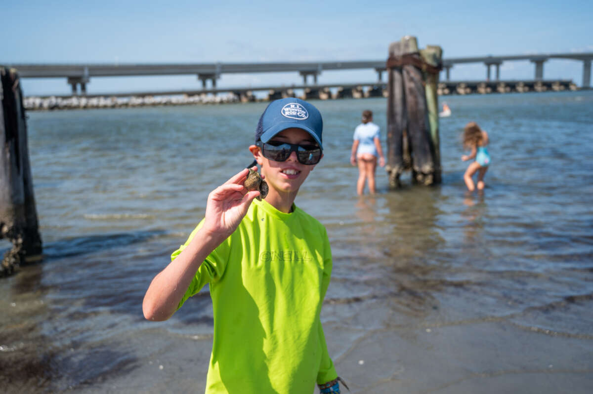 A boy with a blue hat and bright green sun shirt holds hermit crab.